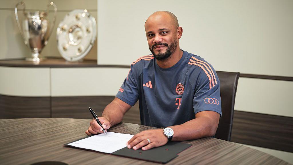 Vincent Kompany sits at a table and signs a piece of paper
