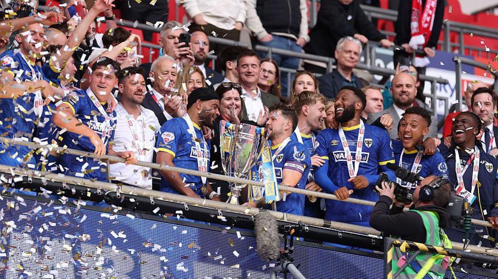 AFC Wimbledon players celebrate with the League Two play-off final trophy