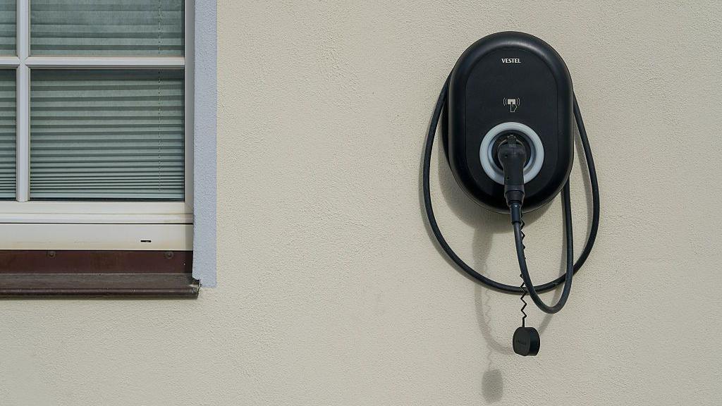 An EV car charger, a black box with a hose, connected to a cream exterior wall on a residential property.