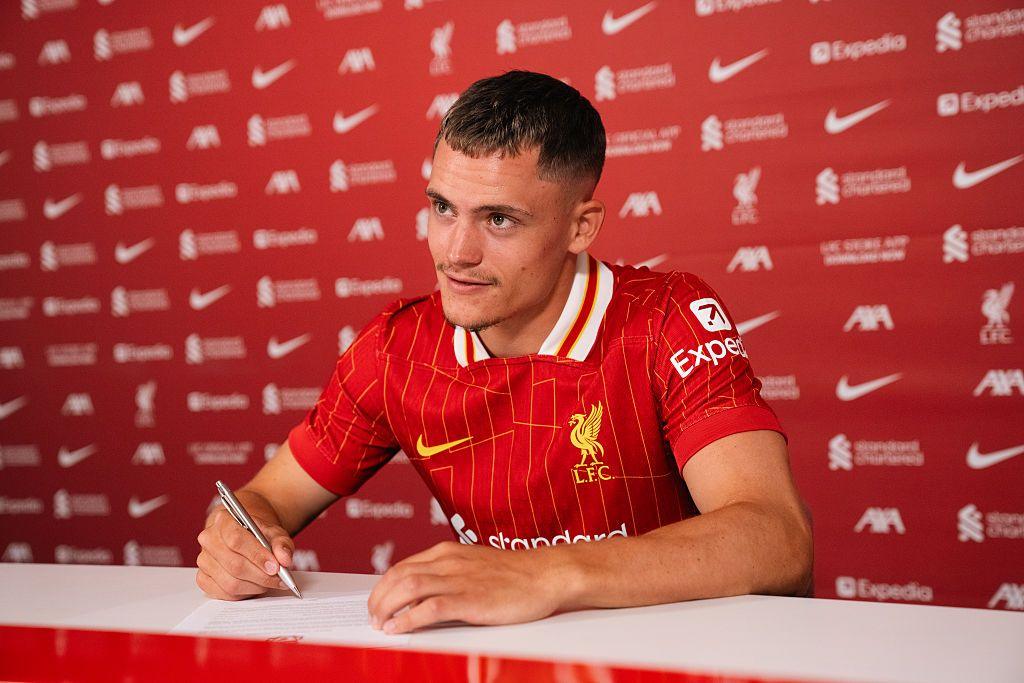 Florian Wirtz smiles while signing a contract after finalising his transfer from Bayer Leverkusen to Liverpool