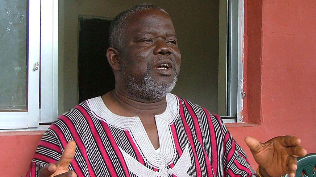 An archive shot of Prince Johnson talking to journalists from 2008. He is wearing a read-black-and-white striped shirt with an embroidered neckline. 