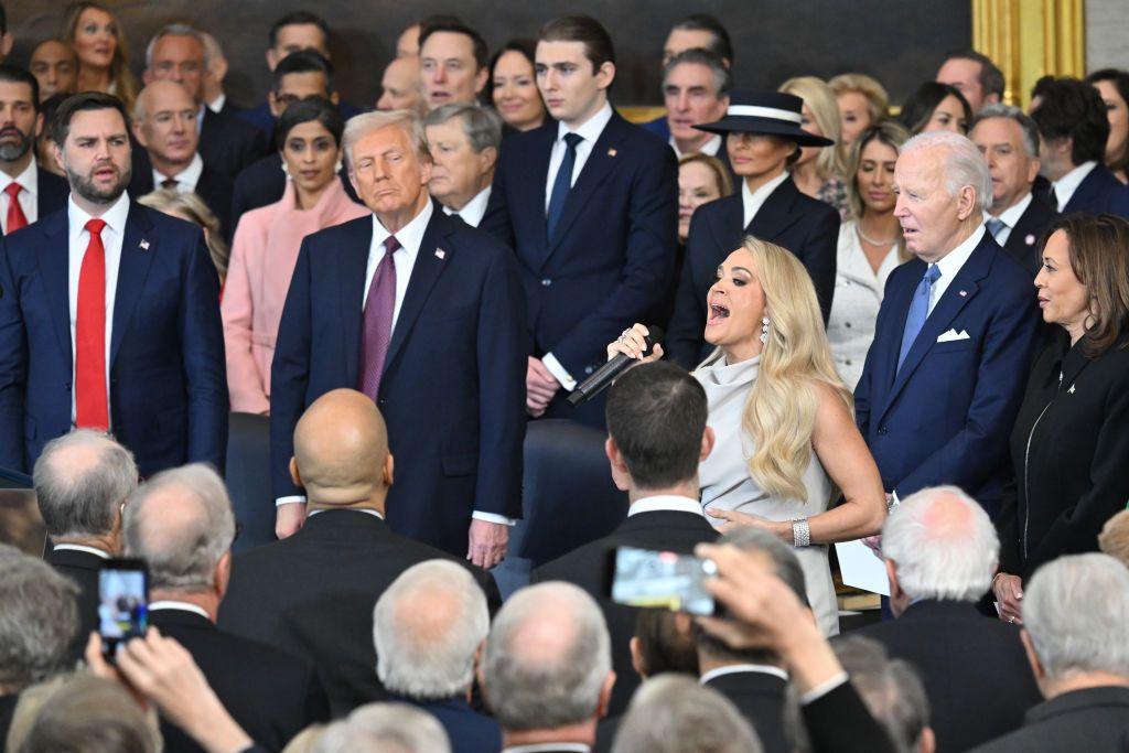 Carrie Underwood, dressed in a silver dress, sings surrounded by people - including Donald Trump, Joe Biden and Kamala Harris, in suits