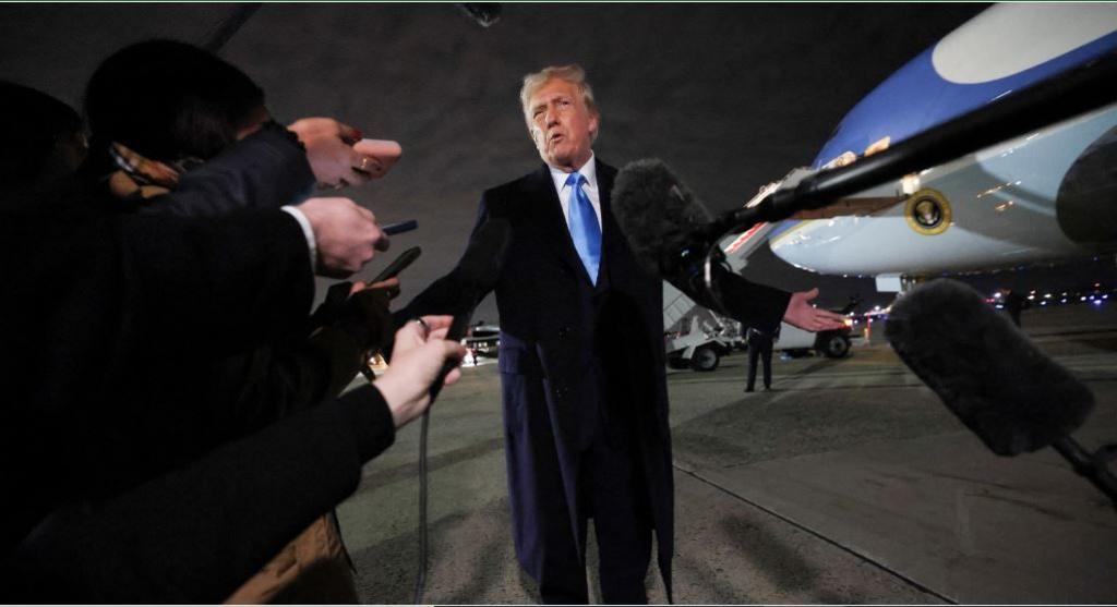 President Donald Trump is interviewed at night by reporters on the runway beside Air Force One