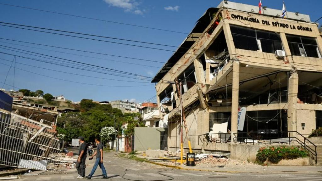 People walk past a collapsed building, in the aftermath of earthquakes in La Guaira, Venezuela