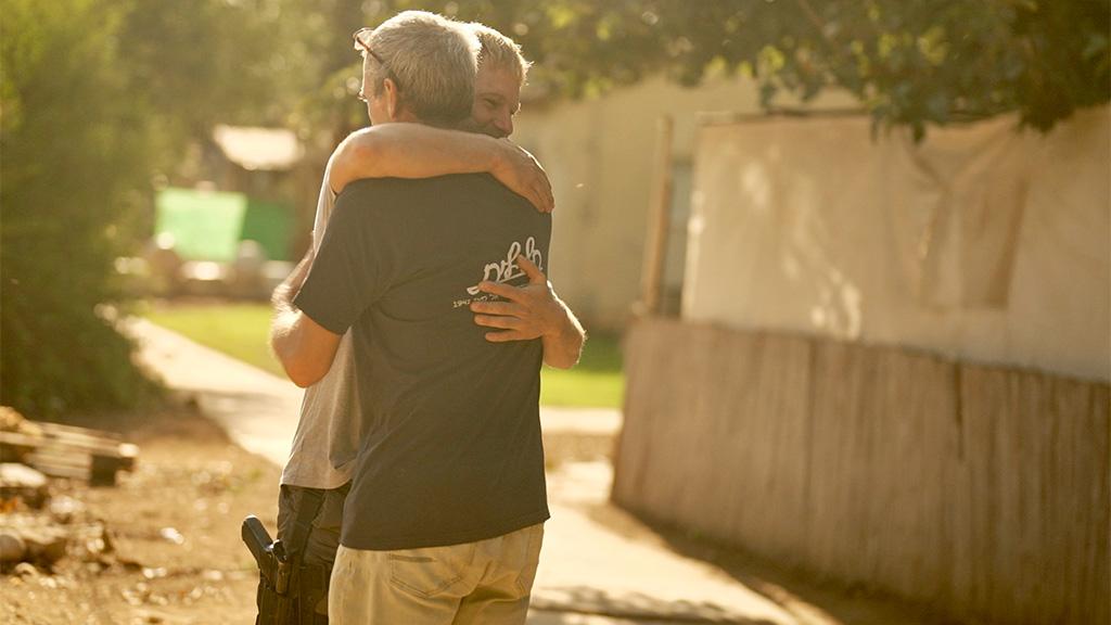 Ido and his son Avichai hug. Avichai carries a gun in a holster