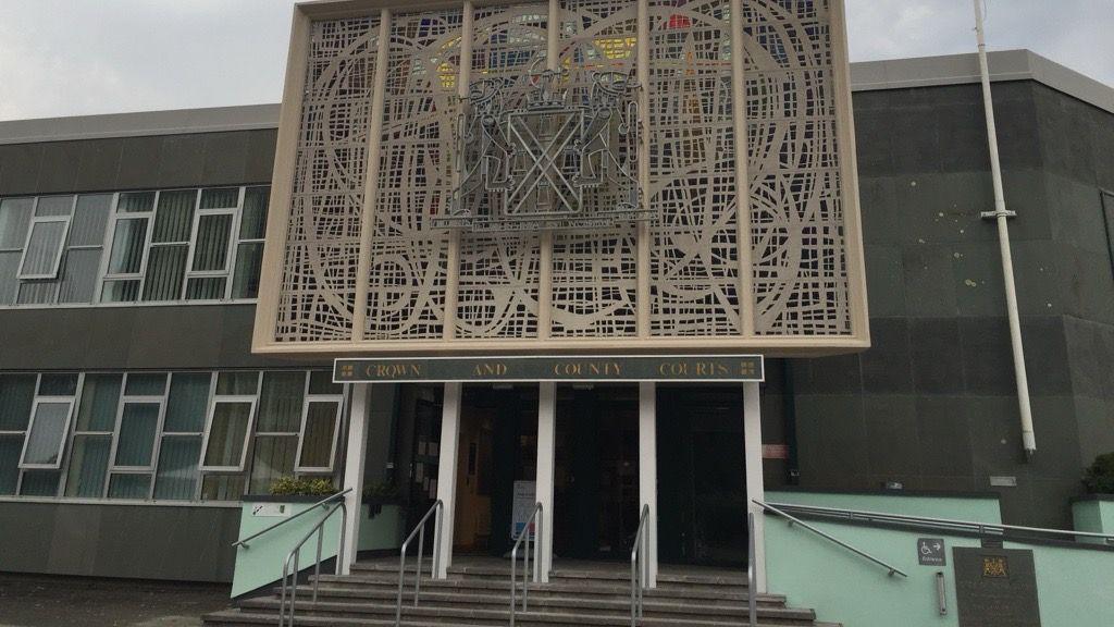 A two-storey building with a sign above the entrance reading: Plymouth Crown and County Courts. There are four entrance doors with steps leading up to them. Above the sign is a large decorative design of wrought stone work.