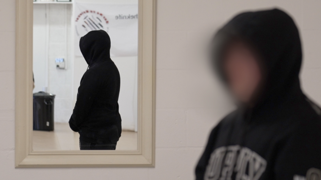 Alfie, whose identity is not being revealed, is wearing  a black hooded top and is stood inside a room with his reflection visible in a mirror. HIs face is blurred and he has his hood up.