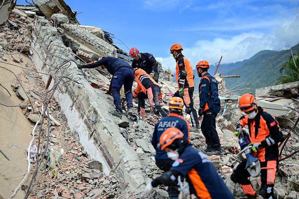 Rescuers wearing orange helmets and navy and orange uniforms use manual tools to search for rescuers in La Guaira.