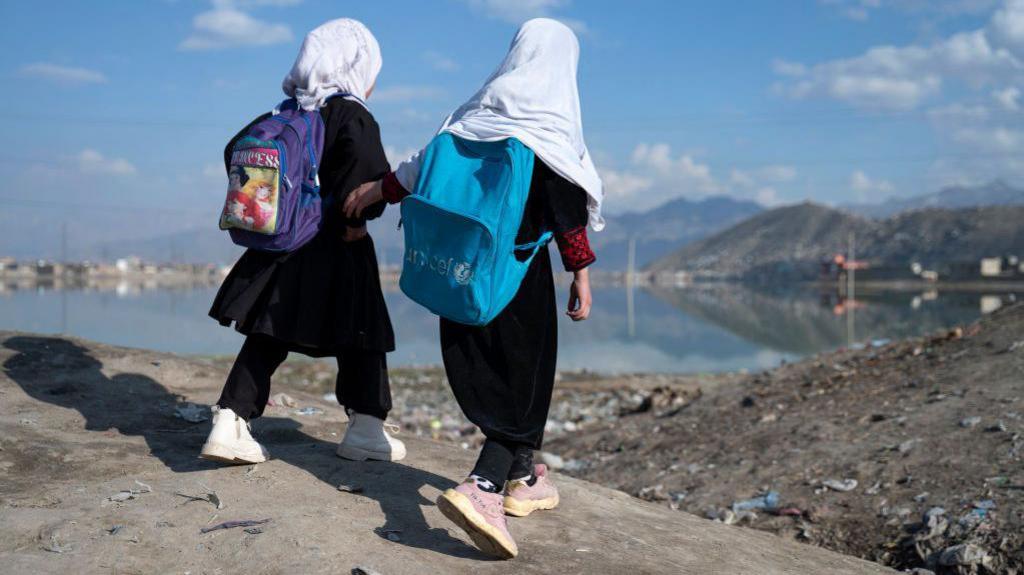 Two girls walking with school backpacks.