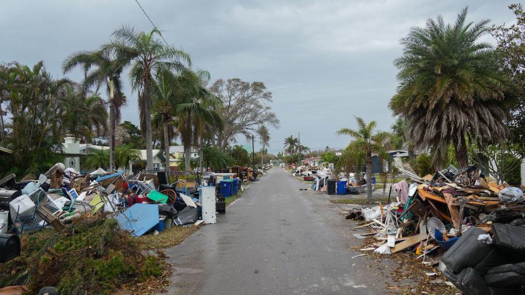 street in florida, lined with broken chairs, buildings and debris from storm.