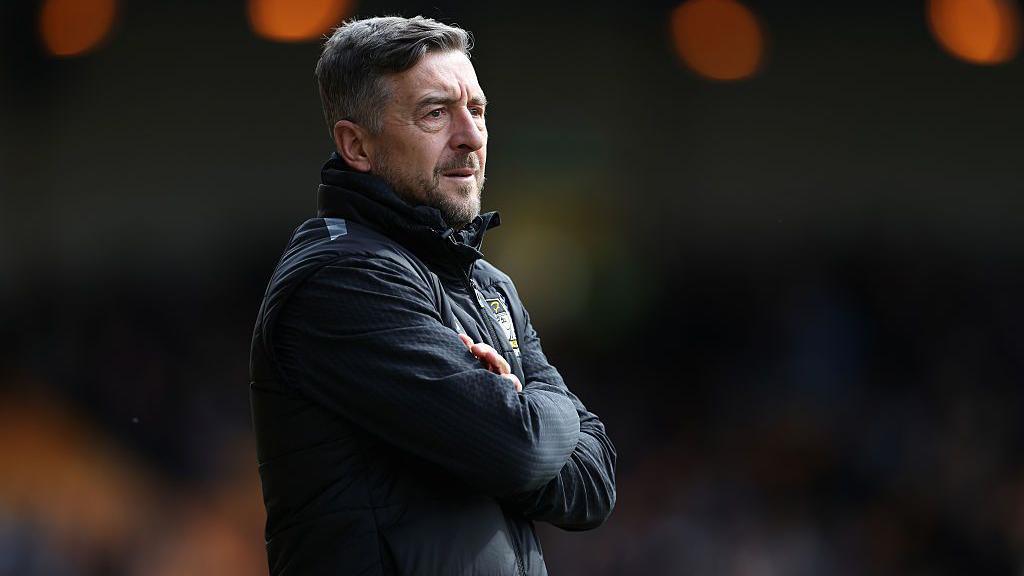 Port Vale boss Jon Brady stands on the touchline with folded arms