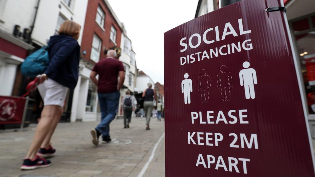 People walk past a social distancing sign