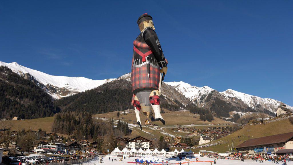 A Scottish Piped Piper hot air balloon flying in a mountain range.