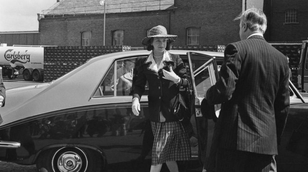 Princess Benedikte, wearing a small hat and black jacket, steps out of a car