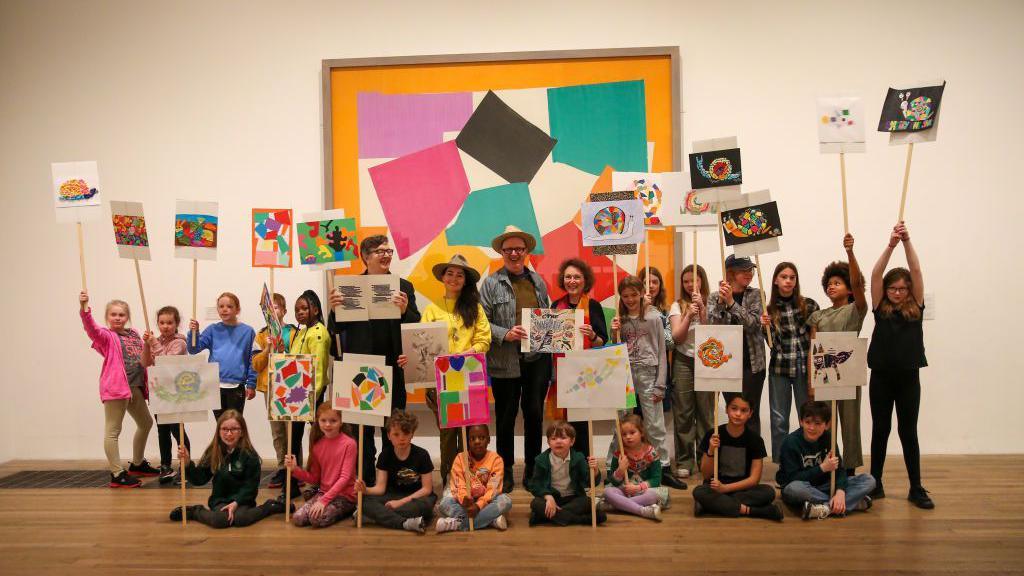 a lot of children and some adults holding drawings up in front of the artwork The Snail by Henri Matisse.