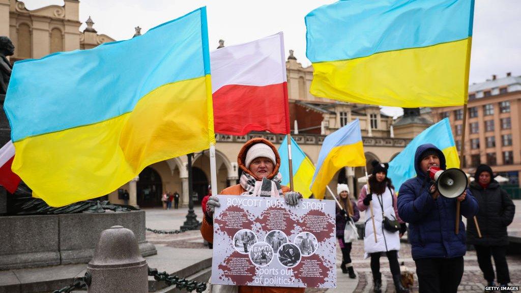 A woman holds up a banner pretesting against Russian sport with Ukrainian and Polish flags flying