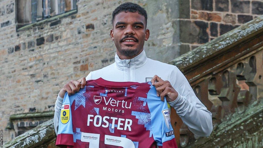 Lyle Foster holding up a Burnley FC shirt bearing his name.