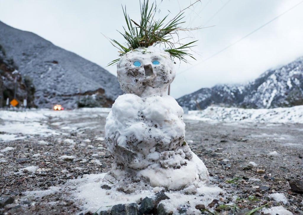 A snowman stands against a background of California mountains