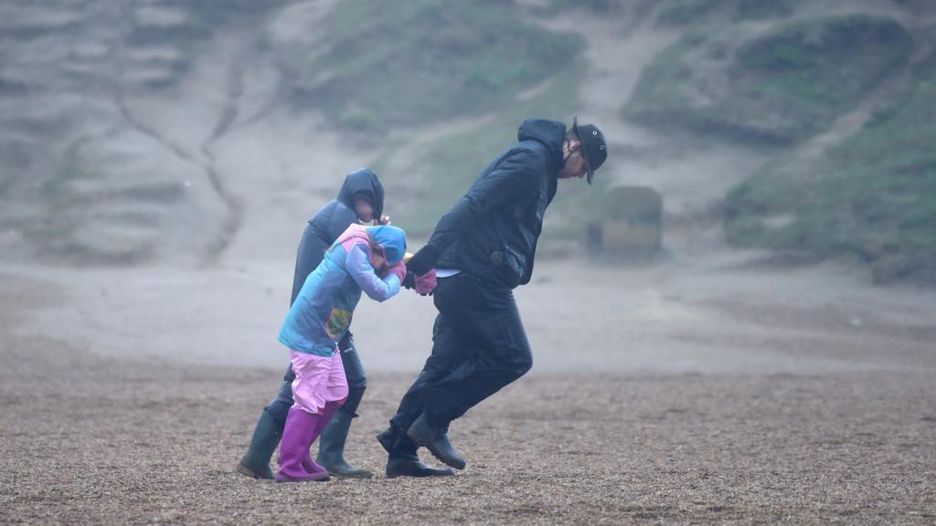 A man and children walk against the wind as Storm Ciara arrive