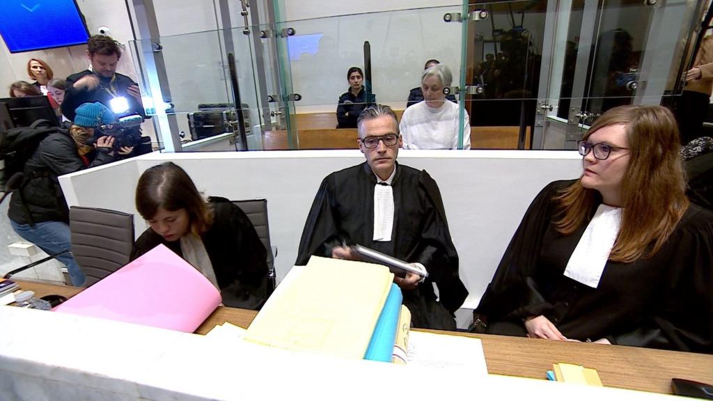 Monique Olivier (rear, in white top) in court