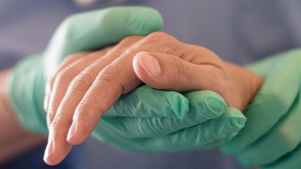 Medical professional wearing gloves holding a patient's hand