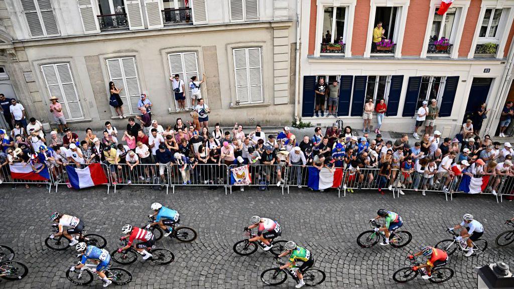 People climb on window-ledges to watch cyclists during the Paris Olympics