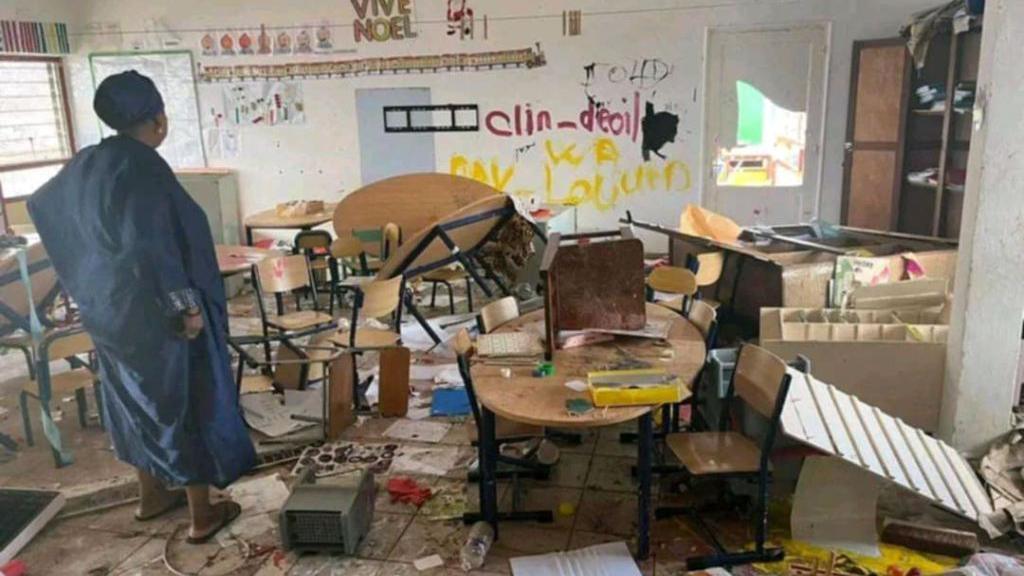 A damaged classroom in Mayotte shows tables overturned and children's art on the floor. A woman looks at the scene - with a "Vive Noel" sign still visible on one of the walls.