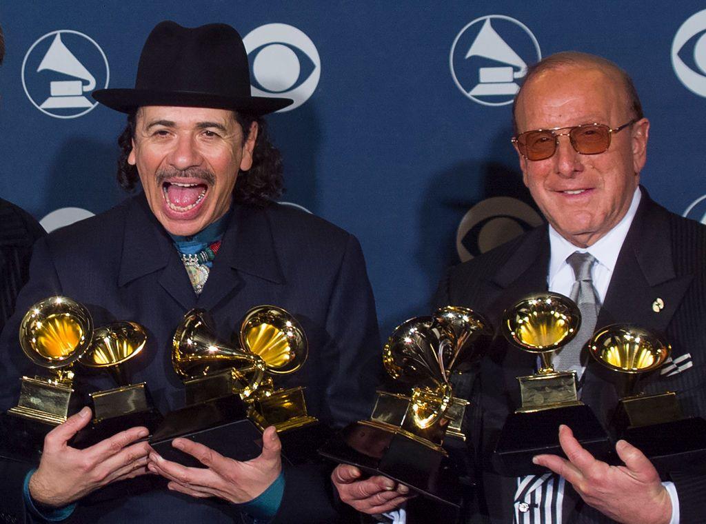 Clive Davis and Santana celebrate their success at the 2000 Grammy Awards, they are both wearing black suits and holding several Grammy trophies each.