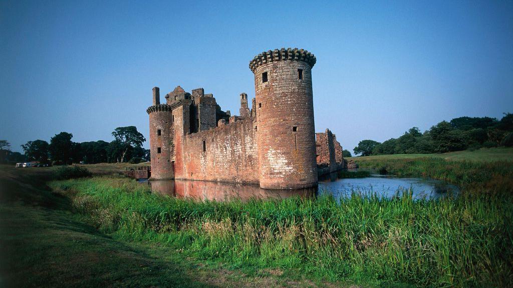 Caerlaverock Castle in Dumfries and Galloway, a triangular ruined sandstone castle surrounded by a moat and grass and trees