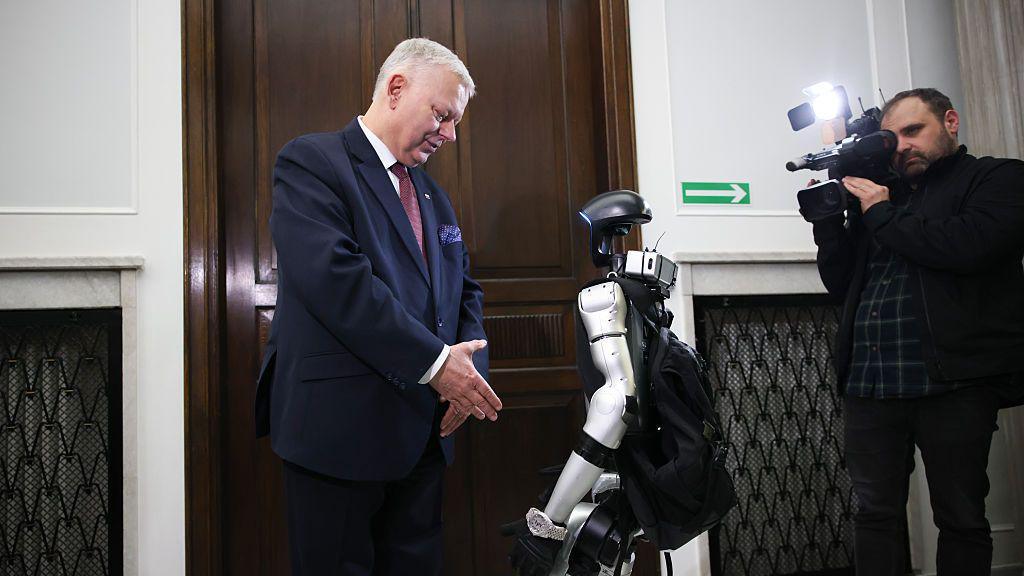 Edward the robot meeting a polish mp, with a camera person filming them.