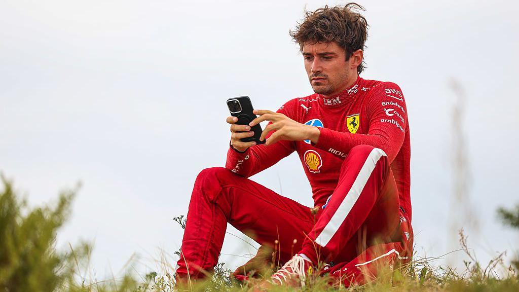 Ferrari's Charles Leclerc sat on sand dunes after retiring from the Dutch Grand Prix, while using a mobile phone