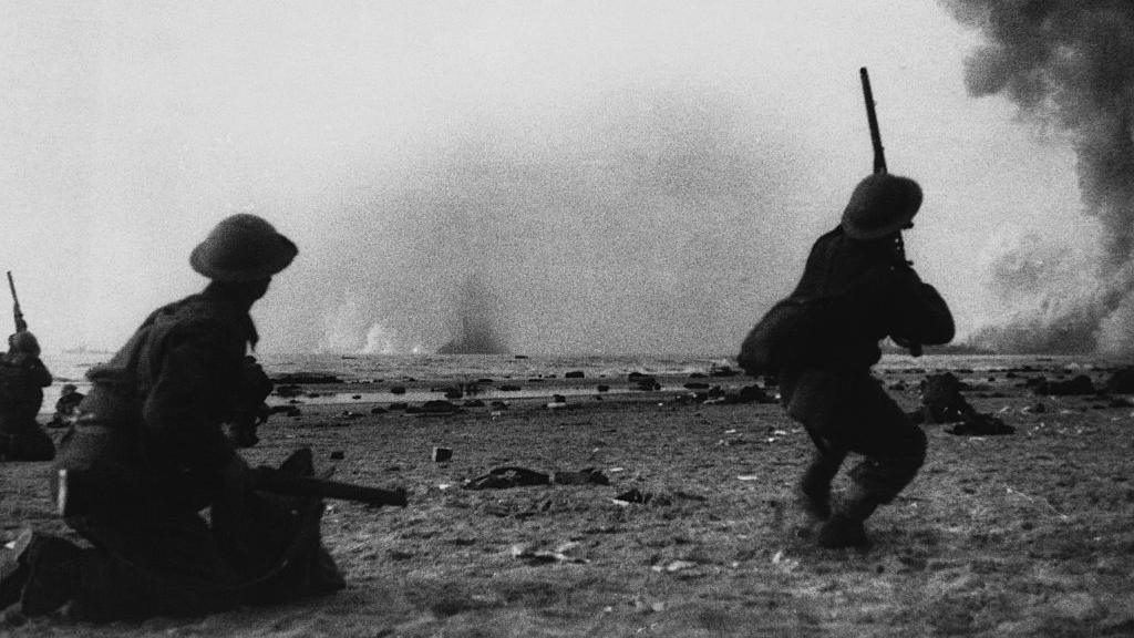 Two British soldiers from World War Two fight with explosions in the distance.