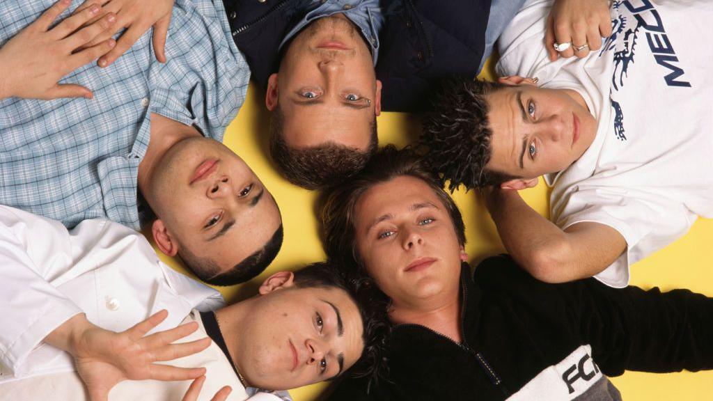 A photo of the boyband Five in 1997 shows all seven members dressed casually, lying in a star formation on a bright yellow floor