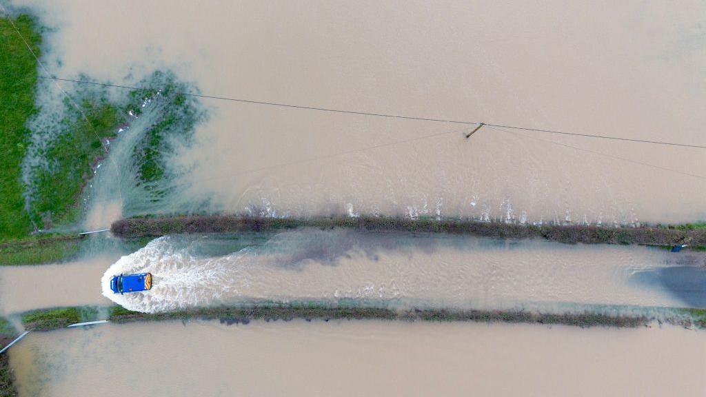 A car navigates a flooded road after the River Rother burst its banks on 5 January 2024 near Petworth, England.