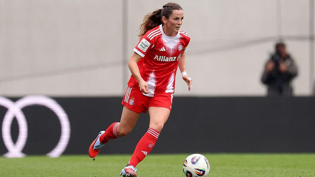 Tuva Hansen in action for Bayern Munich. She has dark hair, tied back, and has the ball at her feet. Bayern's kit is red with white accents.