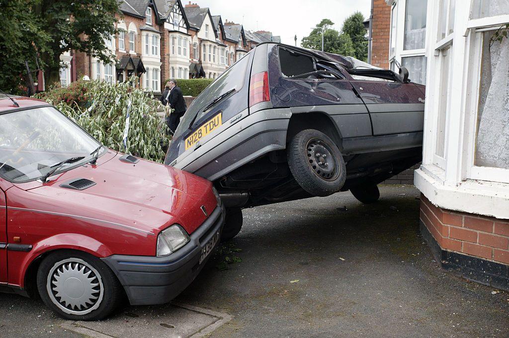 A damaged car rests upon the side of a house