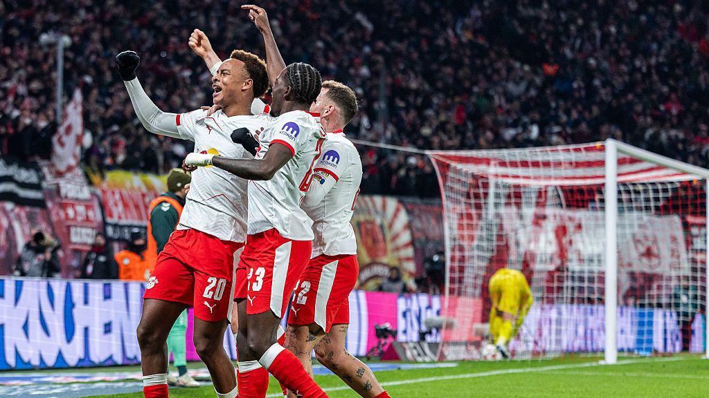 RB Leipzig players celebrate Assan Ouedraogo's goal against Werder Bremen. They are wearing white shirts with red shorts and socks.