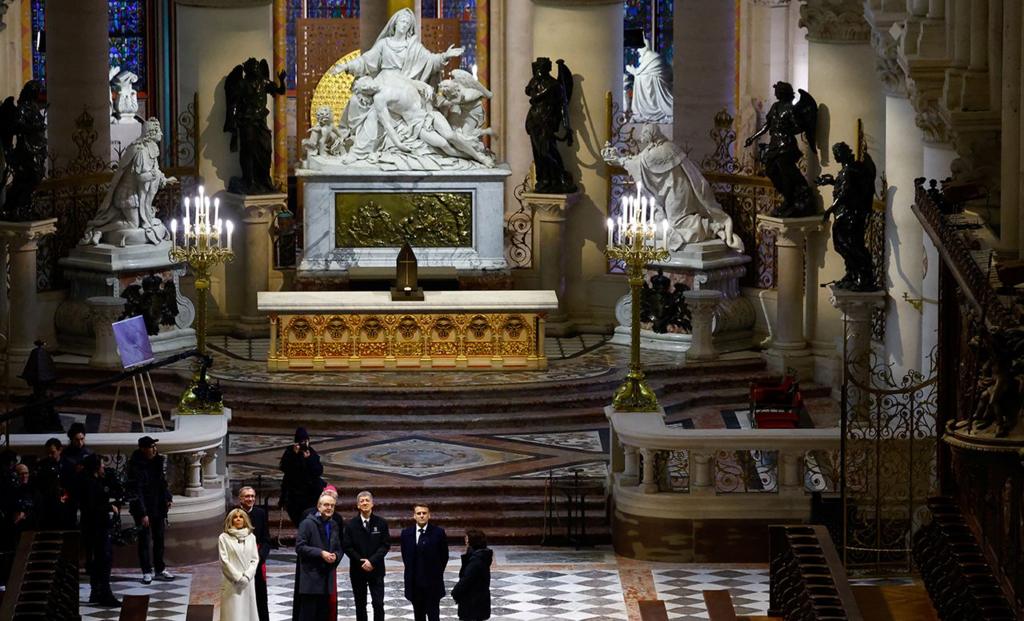 French president Emmanuel Macron standing inside Notre Dame Cathedral, while surrounded by other people