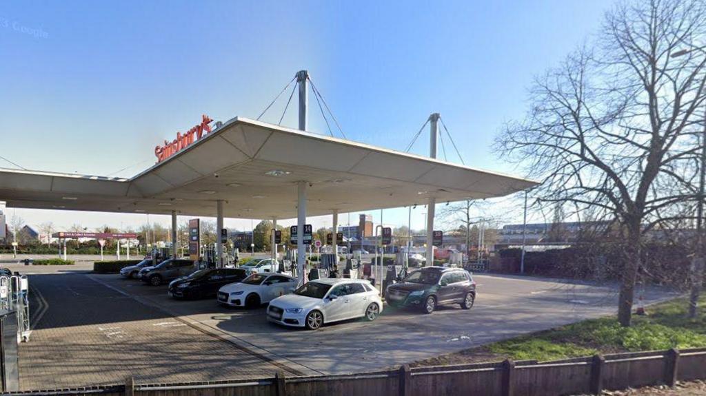 The outside of Sainsbury's petrol station in Farnham with cars at all pumps and a blue sky