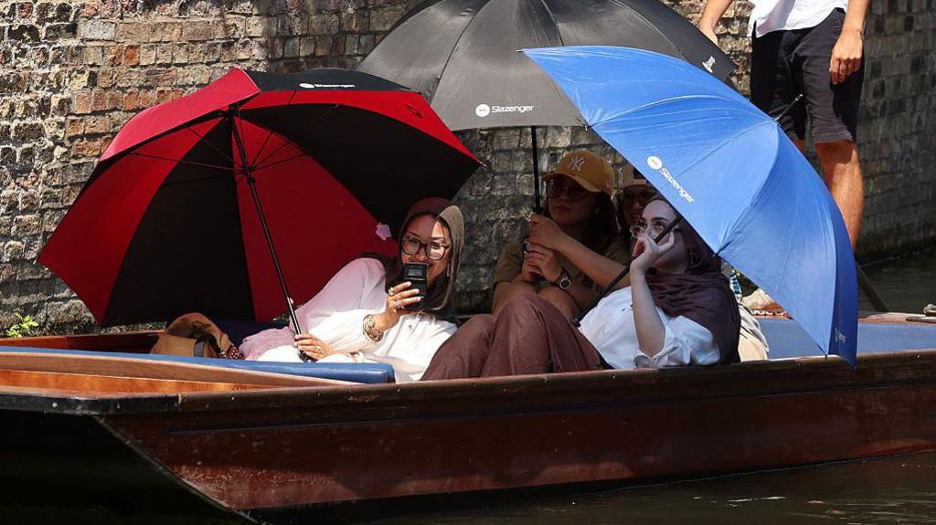 Three women shelter from the sun beneath umbrellas as they take a punt ride along the River Cam, during a heatwave, in Cambridge.