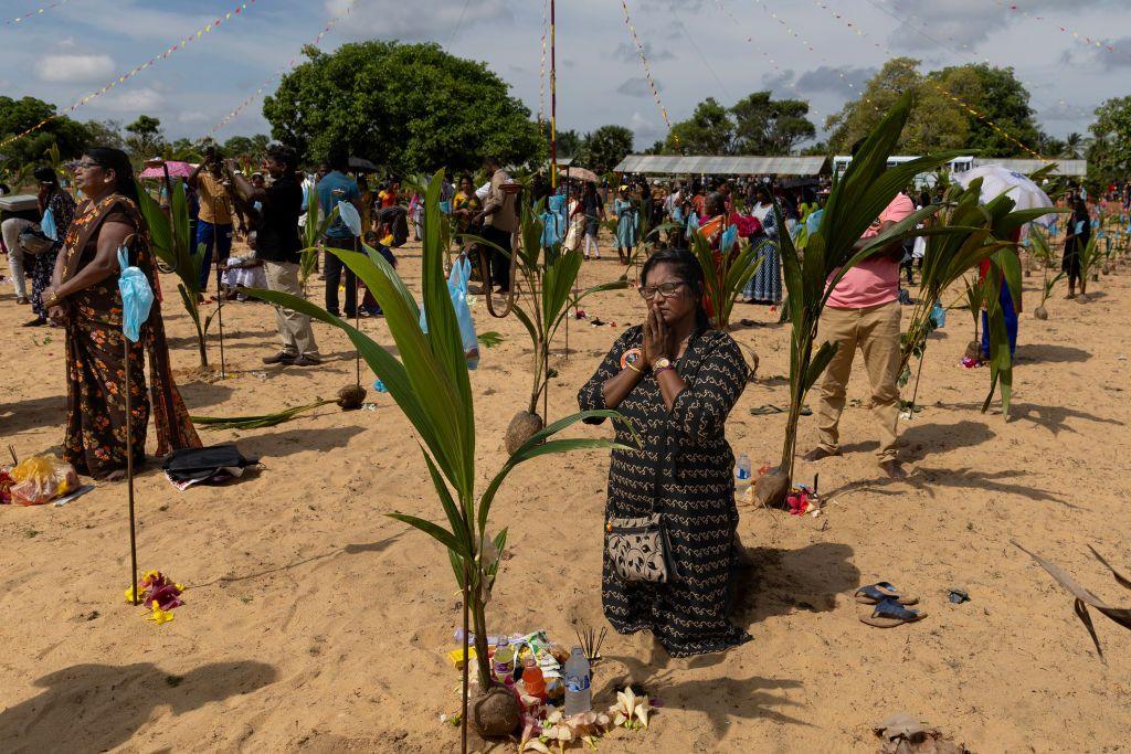 A woman on her knees praying among others who are standing sombrely