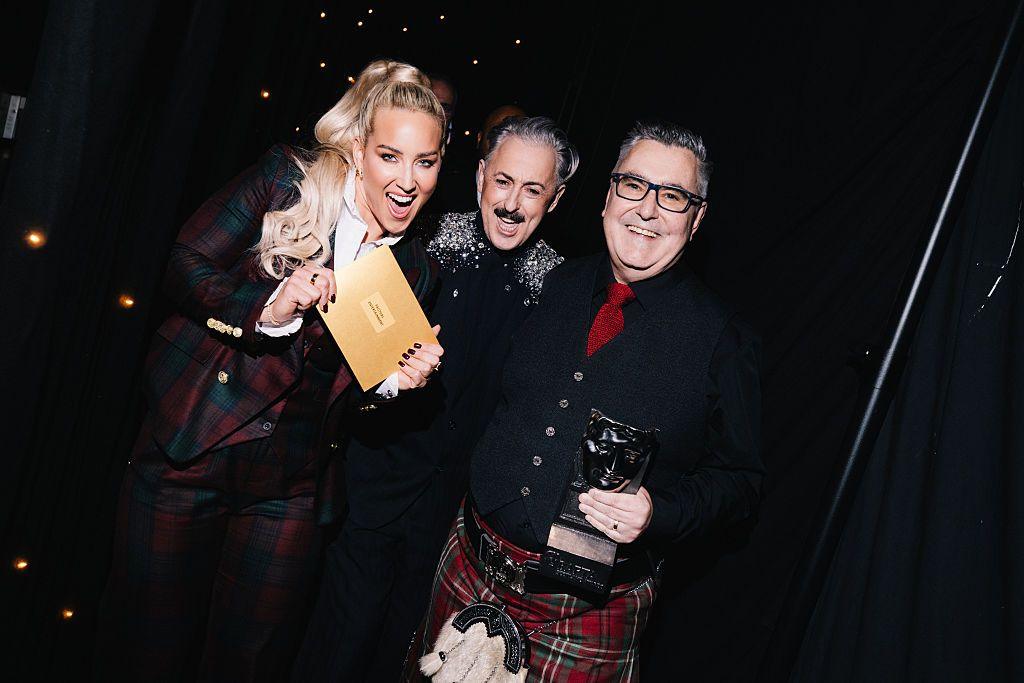 A blonde woman showing off an award, standing next to two men