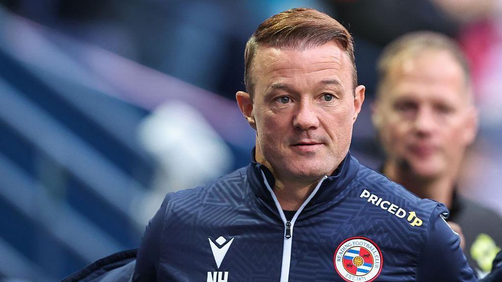 Reading boss Noel Hunt looks on at a game for his side while wearing his blue Reading tracksuit