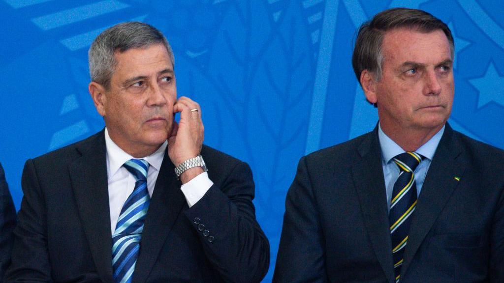 Braga Netto, wearing a suit and tie, scratches his face as he and Jair Bolsonaro, look on during a government event in 2020