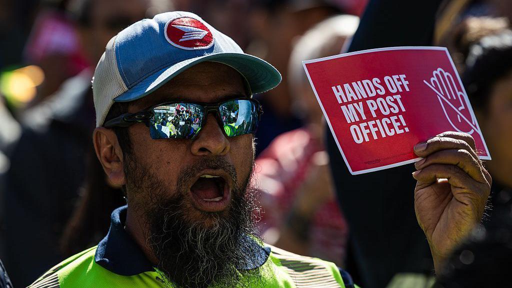 A striking protester holds a sign saying 'hands off my post office' during a rally in October