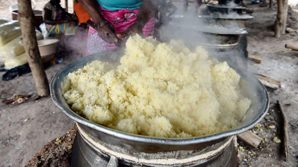 A woman prepares attiéké in a large steel pot