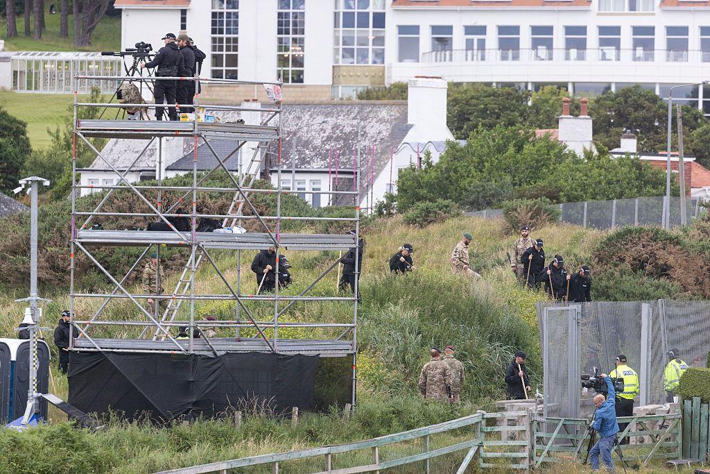 Snipers stand on scaffolding with Turnberry resort in the background. There are several police and military personnel in the shot as well as a metal fence in the right of the frame.