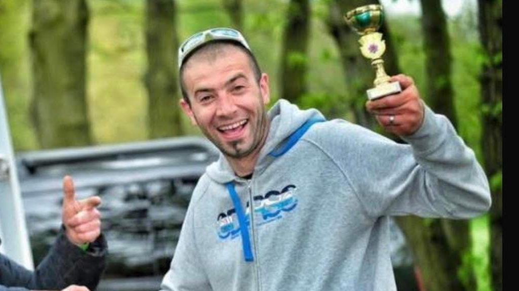 Wojtek Rozmus wearing a grey jumper with glasses on his head holding up a trophy 