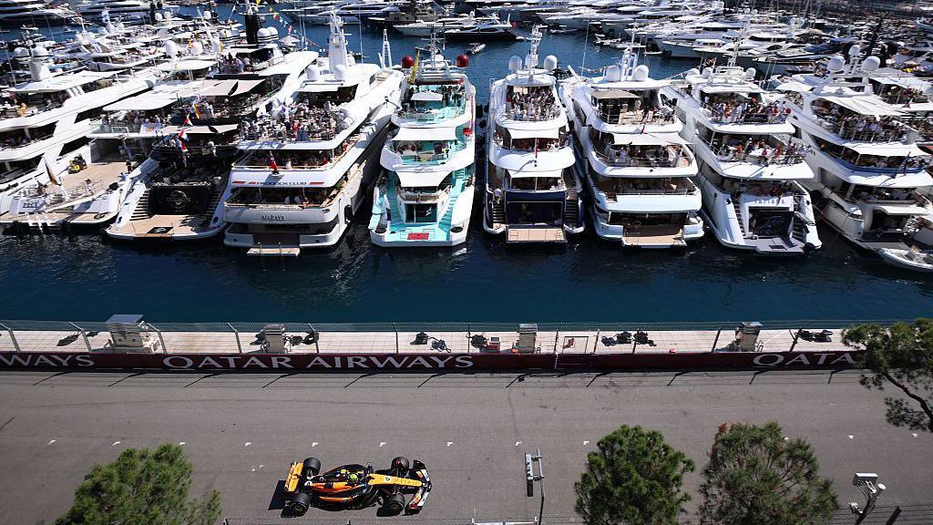 Lando Norris on track in Monaco drives past yachts in the harbour 