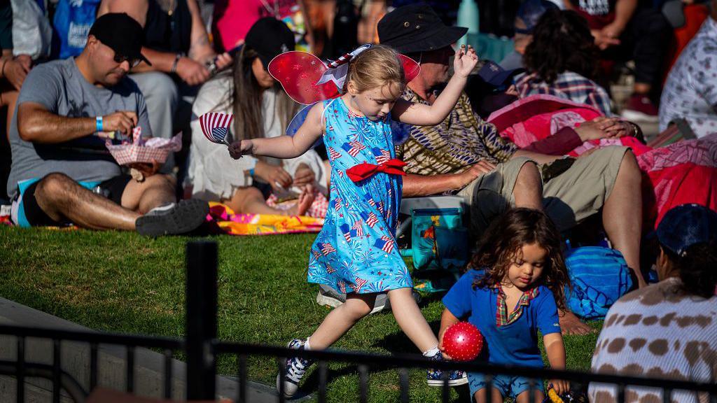 Children with patriotic outfits dance amidst large crowds celebrating Independence Day at the Pier Plaza Festival & Carnival, after the Huntington Beach.